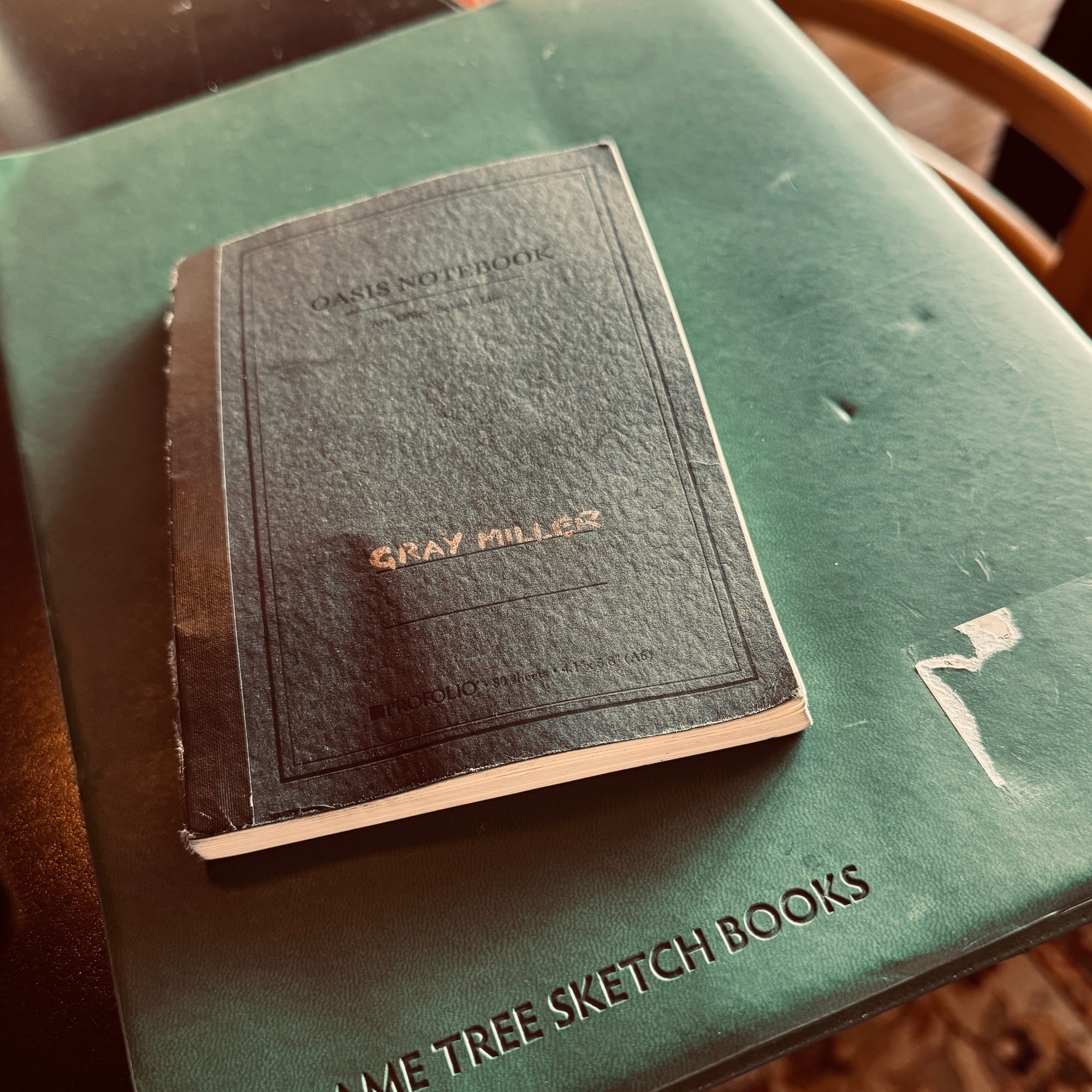 A small black notebook resting on top of a large green sketchboo