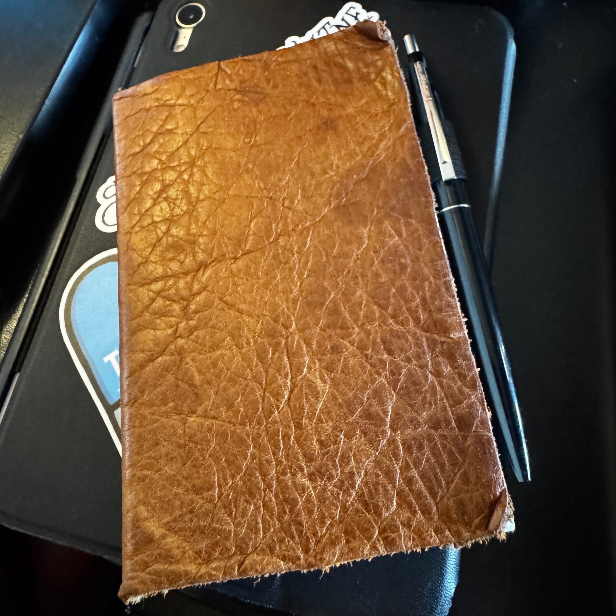 A brown leather pocket-sized notebook with a black pen clipped to the side. 