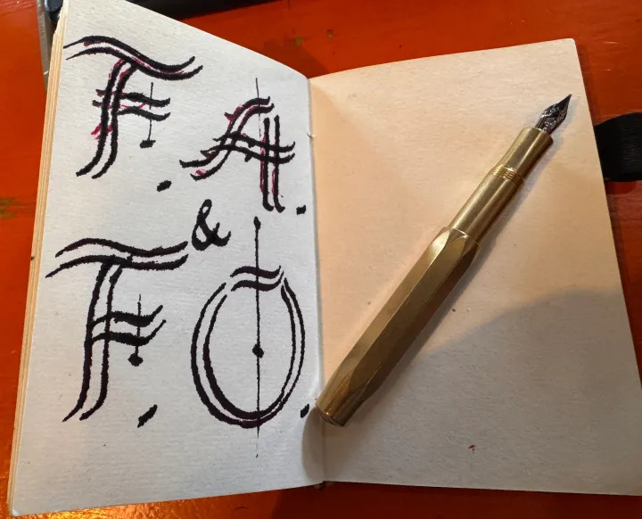 A small notebook with the letters FAFO in calligraphy on one page and a brass Kaweco fountain pen on the other